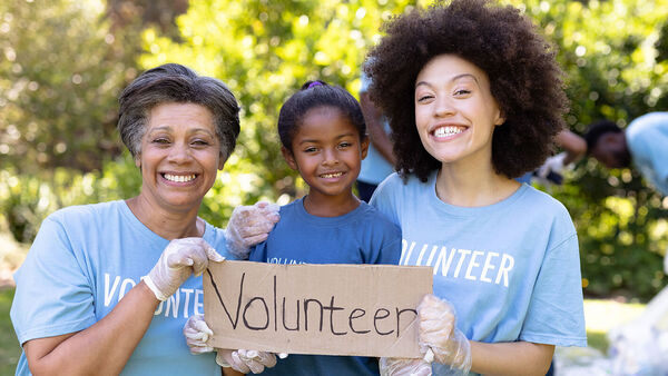 Three people of various ages holding Volunteer sign
