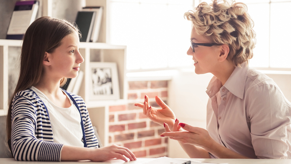 Woman and a girl sitting facing each other speaking.