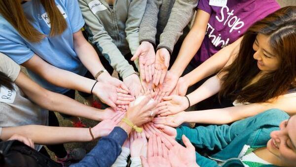 Group of students with all hands in the center like a circle with someone placing something in their palms