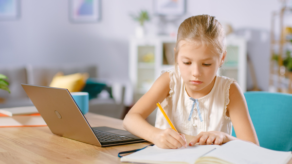 Younger student working on a laptop and writing on a piece of paper.