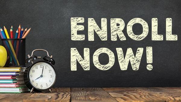 Words says enroll now. There is a desk with clock, apple, and pencils on it.