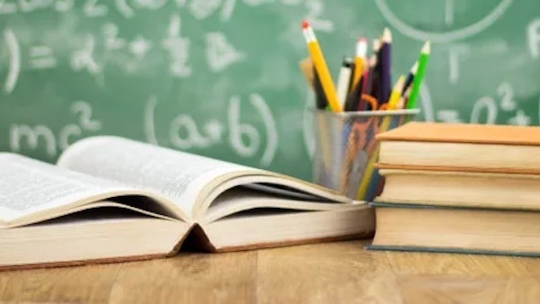 Open book with pencils on a desk. Blurry chalkboard in the background.