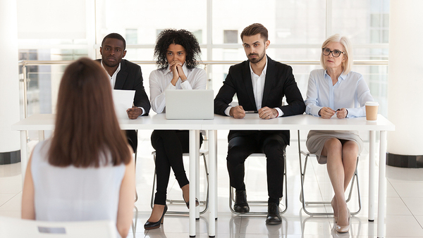 Backside of person in chair with a panel of people interviewing