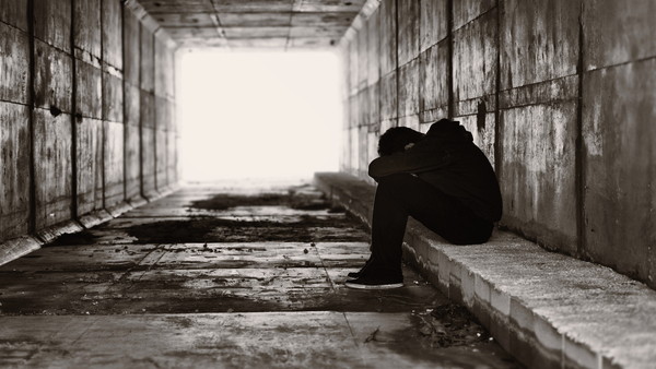 Greyscale image of teen with head in hands and knees in a tunnel