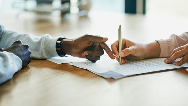 Two sets of hands with one pointing to a piece of paper and the other holding a pen.